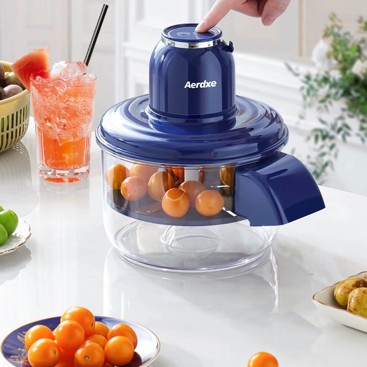 Blue Aerdx juicer with oranges on a kitchen counter, surrounded by fruits and a drink.